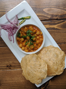 Indian Chole / Chana Bhatura ( Chickpea Curry ) with Bhatura ( puffed flat bread ) on a plate with pickled onions and green chilies 
